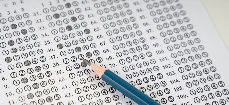 Blue pencil rests beside filled answer sheet. Circular choices mark student responses clearly. Paper shows rows of numbers and symbols. Test-taker focused, deliberate, concentrated