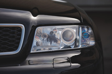Close up front view of modern clear lens projector headlight assembly on black luxury sports car. © Octavian