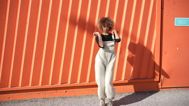 A Joyful Woman Energetically Dancing Against a Beautiful and Vibrant Orange Wall
