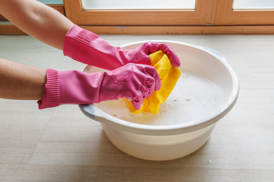 Hands in rubber gloves washing a cleaning cloth in a basin with soapy water during household cleaning, floor washing and everyday housework at home.