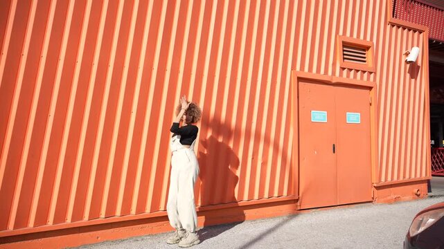 A young person striking a pose in front of a vibrant and energetic orange wall behind them