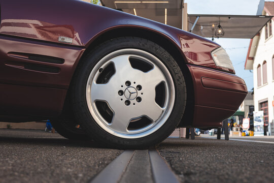 Lindau, Switzerland, August 9, 2026. Low angle view of an AMG Monoblock alloy wheel on a dark red 1990s Mercedes-Benz R129 SL roadster.
