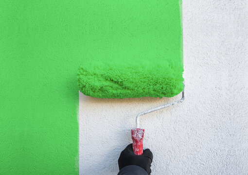 hand holds paint roller and painting a wall