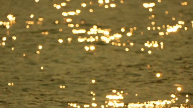 Golden water glimmers with warm solar highlights across a calm surface at dusk. Rack focus shot transitions from blurry bokeh to sharp texture.