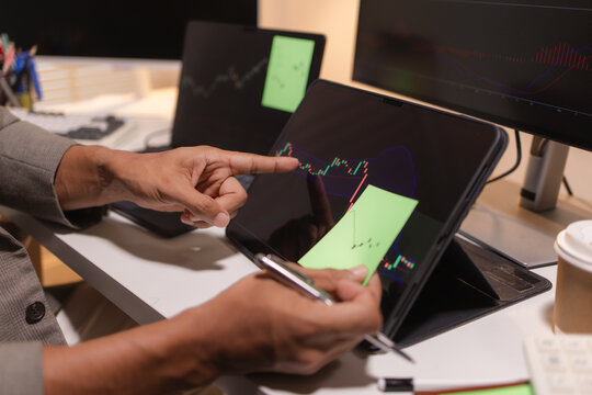 Professional stock trader reviewing market charts with sticky notes across multiple monitors, laptop, and tablet to analyze price trends, plan trading strategies, and manage investment decisions.