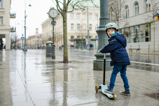 Young child rides a kick scooter through the city during falling snow. Active outdoor childhood and urban transportation in cold winter weather.