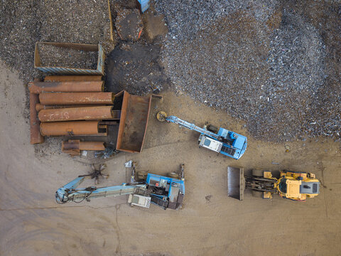 Aerial view of heavy machinery and excavators working in a scrap metal yard with piles of metal and large rusty pipes in Agnesberg, Gothenburg, Vastra Gotaland, Sweden.