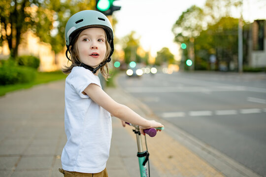 Young boy wearing a safety helmet rides a kick scooter on a city sidewalk. Active childhood, urban mobility and road safety for children.