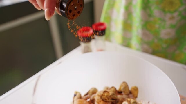 Hand Sprinkles Ground Seasoning over Raw Shrimp and Mussels in a White Bowl on a Kitchen Counter, Showing Fresh Food Preparation and Home Cooking Slow motion