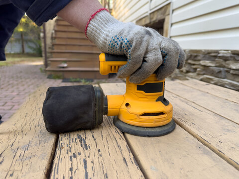 Close-Up of a Hand Using an Electric Sander on Weathered Wooden Surface to Smooth Out Imperfections Before Finishing Touches in Home Renovation Project
