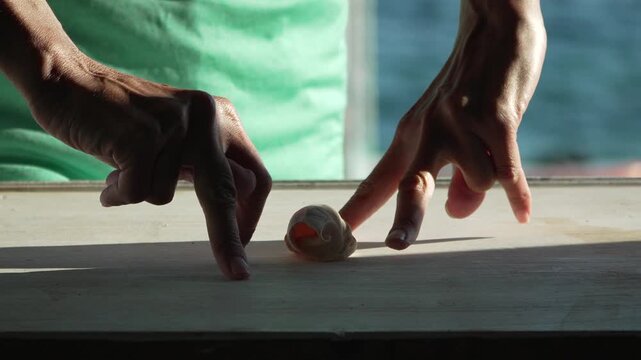 Hands playing playful finger walk game towards seashell on wooden coastal table in static medium shot