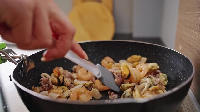 A Hand Stirs Shrimp Squid and Mussels in a Black Wok, Preparing a Fresh Protein Rich Meal in a Home Kitchen for Healthy Eating Slow motion