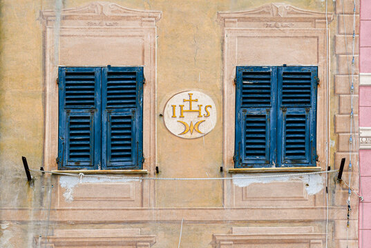 Traditional Ligurian house facade with two dark window shutters and an ancient IHS religious monogram medallion in Camogli, Genoa, Italy