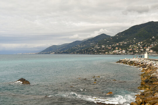 Scenic view of the rocky coast with a white lighthouse and the Gulf of Genoa coastline in the background, Camogli, Liguria, Italy