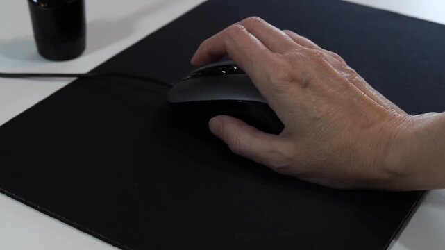 Hand clicks and scrolls on a black wired optical mouse on a mouse pad next to a keyboard