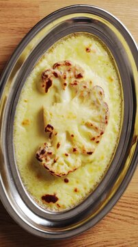 Home cook places baked cauliflower in cheese sauce on table. Baked cauliflower supplies fibre, vitamins and nutrients. Pair baked cauliflower with salad, grains, beans or greens for balanced dinner.