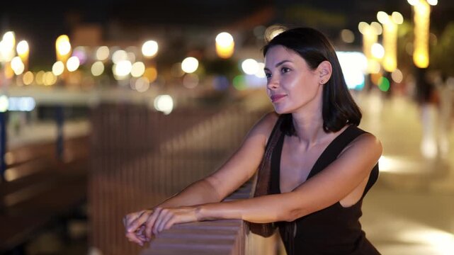 Night walk around old district. Woman put hands on fencing, watching towards beach of Barceloneta from height of pedestrian promenade. Night fell on city 