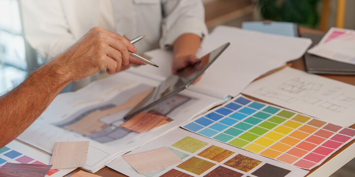 Cropped hands of interior designers selecting color swatches and reviewing tablet for project planning