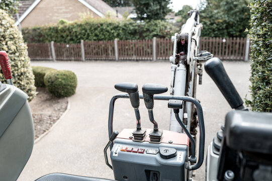 Unusual, drivers view of a small mechanical digger and excavator seen on a housing estate in the UK. The joysticks control the steering and the central levers control the hydraulic arm and scoop.