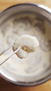 Tweezers hold battered shrimp before frying in hot oil. Battered shrimp shows coating step in seafood cooking tutorial. Feature battered shrimp recipe in food blog, social media reel or video guide.