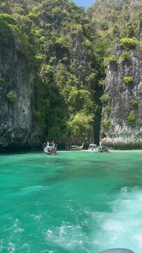 Vertical view of a traditional Thai longtail boat cruising the turquoise waters of the Andaman Sea among dramatic limestone cliffs in the Phi Phi Islands, Thailand.