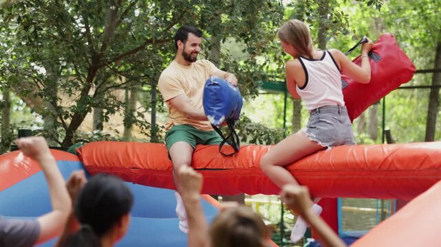 Cheerful guy and girl in an inflatable bags fighting arena at an outdoor amusement park on a sunny summer day. . High quality 4k footage