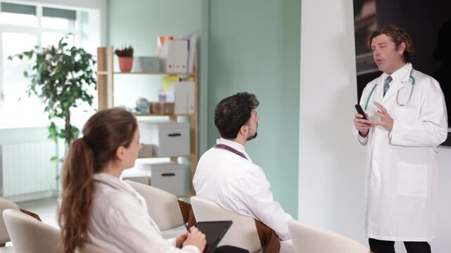 Male doctor lecturer communicates and addressed to attendees, controls projector using remote control. Professional meeting, medical council