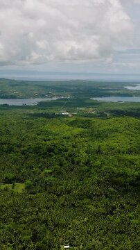 Expansive green landscape with tropical hills, lakes, and a distant sea horizon beneath scattered clouds. Camotes, Philippines.