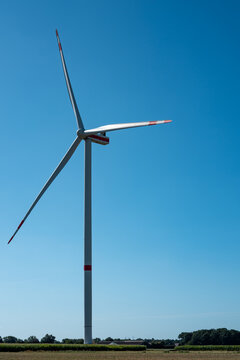 Wind turbine standing tall under a clear blue sky in a rural area during the day