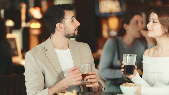 Young couple with mugs of beer in their hands chatting near the bar in a nightclub. High quality 4k footage