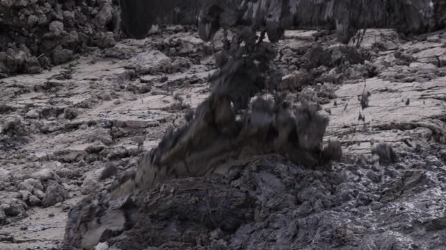 Raw industrial energy and relentless earth-moving force dominate the scene; dark, clumped soil and rugged machinery convey heavy labor and extraction