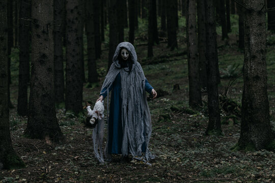 Spooky and scary Halloween themed image in a dark forest with smoke and an eerie woman with a mask. .