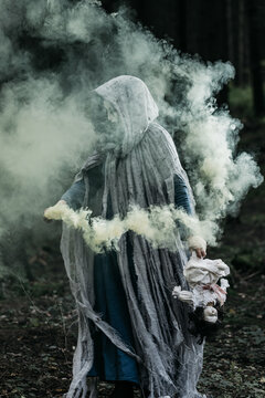 Spooky and scary Halloween themed image in a dark forest with smoke and an eerie woman with a mask. .