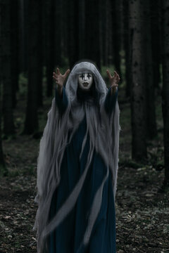 Spooky and scary Halloween themed image in a dark forest with smoke and an eerie woman with a mask. .