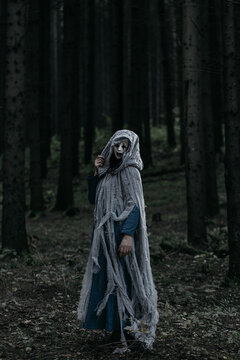 Spooky and scary Halloween themed image in a dark forest with smoke and an eerie woman with a mask. .