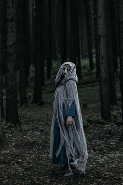 Spooky and scary Halloween themed image in a dark forest with smoke and an eerie woman with a mask. .