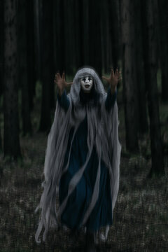 Spooky and scary Halloween themed image in a dark forest with smoke and an eerie woman with a mask. .