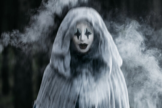 Spooky and scary Halloween themed image in a dark forest with smoke and an eerie woman with a mask. .