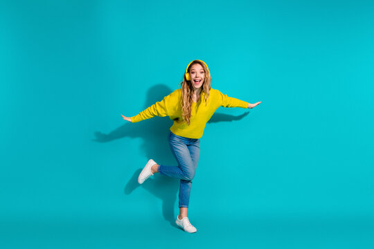 Joyful young woman in a yellow sweater leaps against a blue background showcasing casual fashion lifestyle and energetic playful style in a bright studio setting