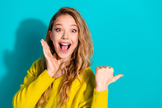 Happy young woman with blonde hair in a bright yellow sweater posing blue background showing excitement joy for lifestyle fashion advertising