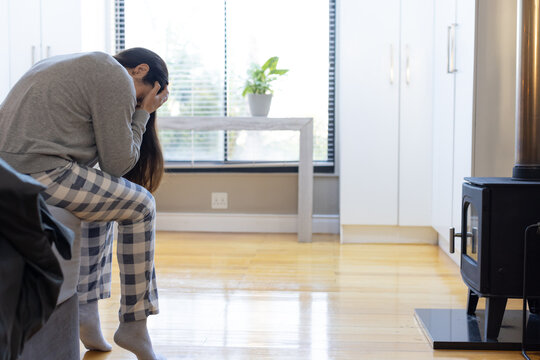 Woman sitting on couch wearing plaid pajama pants holding face in hands at home, copy space
