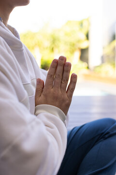 Female pressing palms together at chest while sitting on wooden deck wearing light sweatshirt