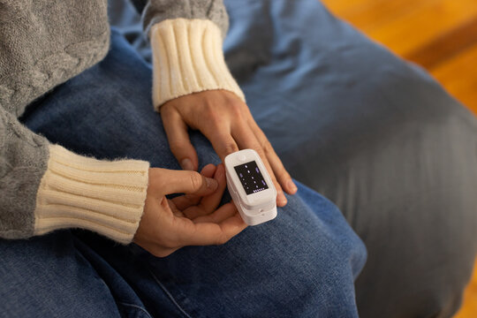 Female sitting on blue sofa wearing gray sweater and jeans, adjusting white pulse oximeter