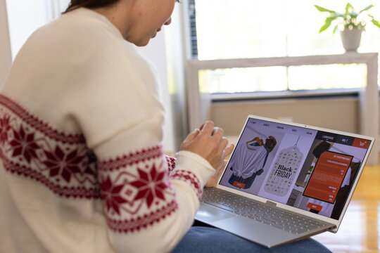 Adult female browsing Black Friday clothing store on laptop at home wearing patterned sweater