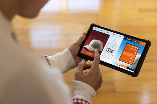 Female wearing white sweater tapping tablet, browsing Black Friday cap with orange buttons on floor