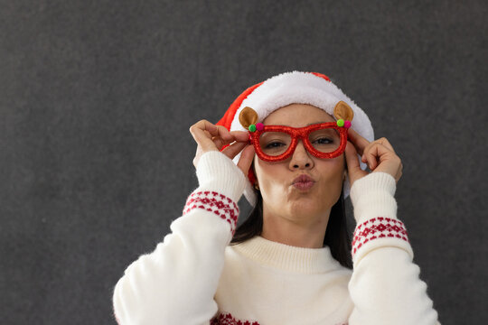 Adult female posing in studio, wearing Santa hat, holding red glitter glasses and puckering lips