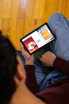 African American male sitting on wood floor in maroon sweater using tablet showing Black Friday cap