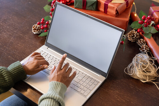 Mature African American woman in green sweater typing on laptop at wood table with wrapped gifts