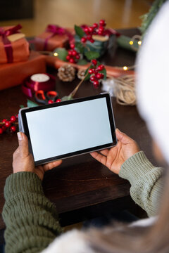 African American woman holding tablet in landscape at wooden table, wrapping gifts with ribbon