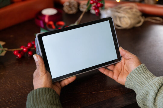 Mature African American woman in green sweater holding tablet in case on wooden table with ribbon